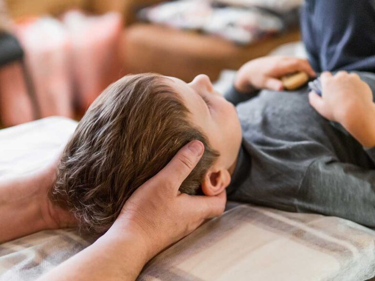 A person gently stretching their back in a sunlit living room with a yoga mat and supportive pillows nearby.